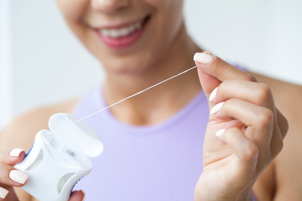 Smiling woman holding dental floss and preparing to clean her teeth