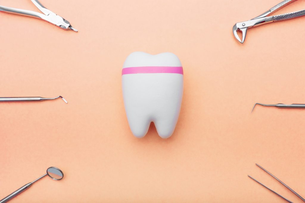 Modern and traditional dental tools surrounding a model tooth on an orange background