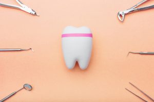 Modern and traditional dental tools surrounding a model tooth on an orange background