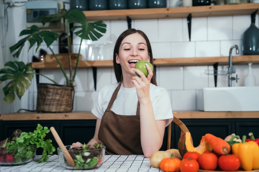 Woman smiling while holding a green apple surrounded by fresh vegetables