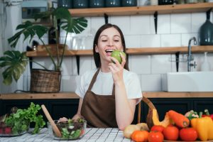 Woman smiling while holding a green apple surrounded by fresh vegetables