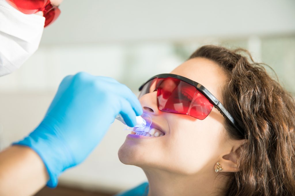 Woman receiving professional teeth whitening with UV light in a dental office