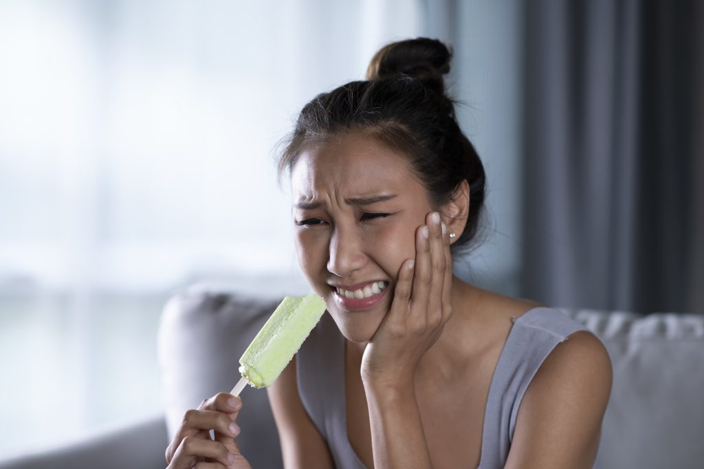 Woman experiencing tooth sensitivity while eating ice cream