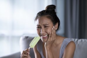 Woman experiencing tooth sensitivity while eating ice cream