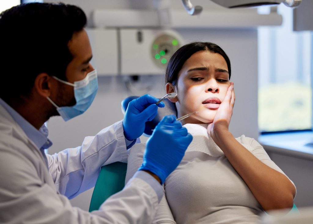Female patient holding her cheek in pain during emergency dental exam